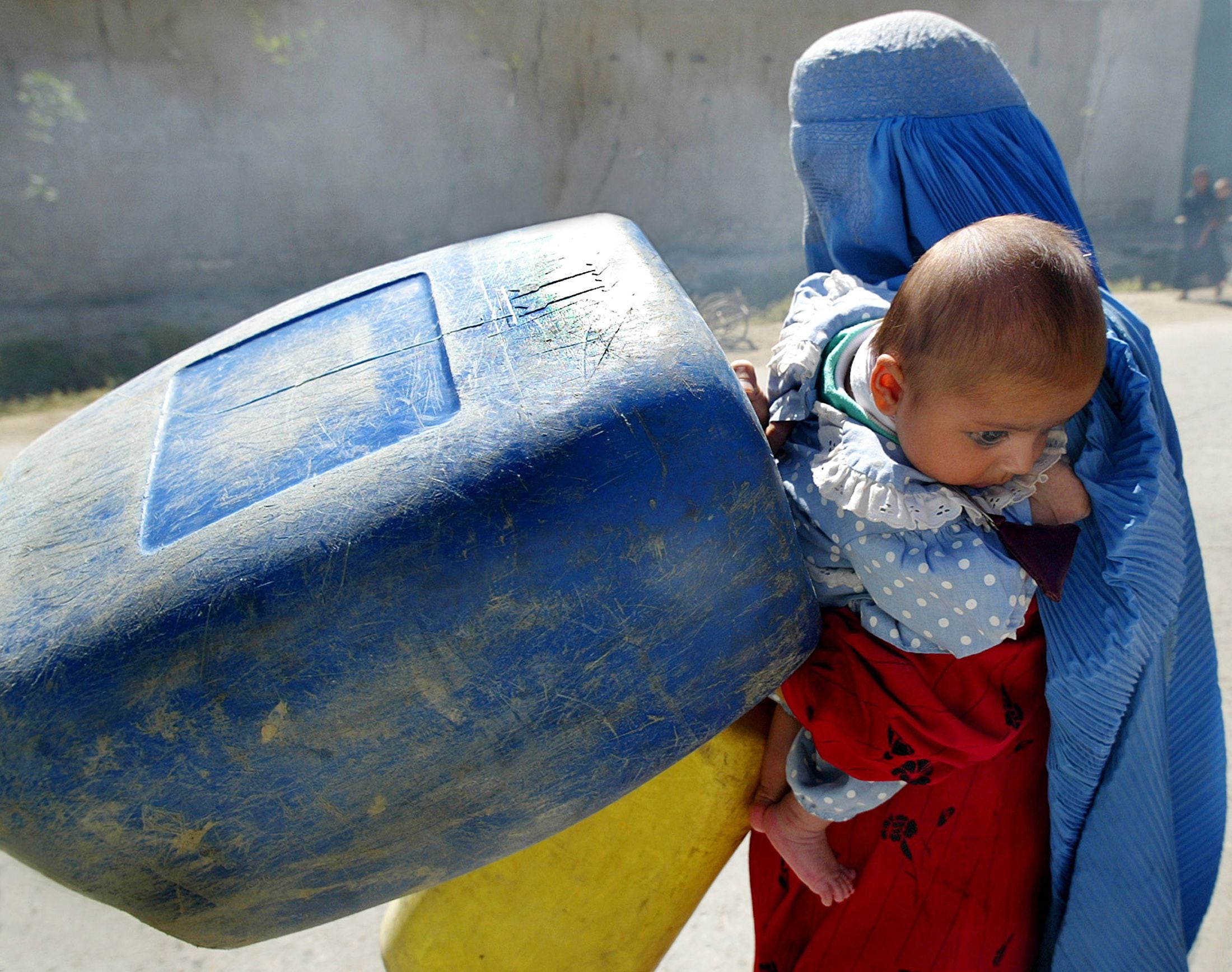 AN AFGHAN WOMAN WALKS WITH BUCKETS TO FILL WITH DRINKING WATER
FROM A MOBILE WATER TANK IN KABUL.