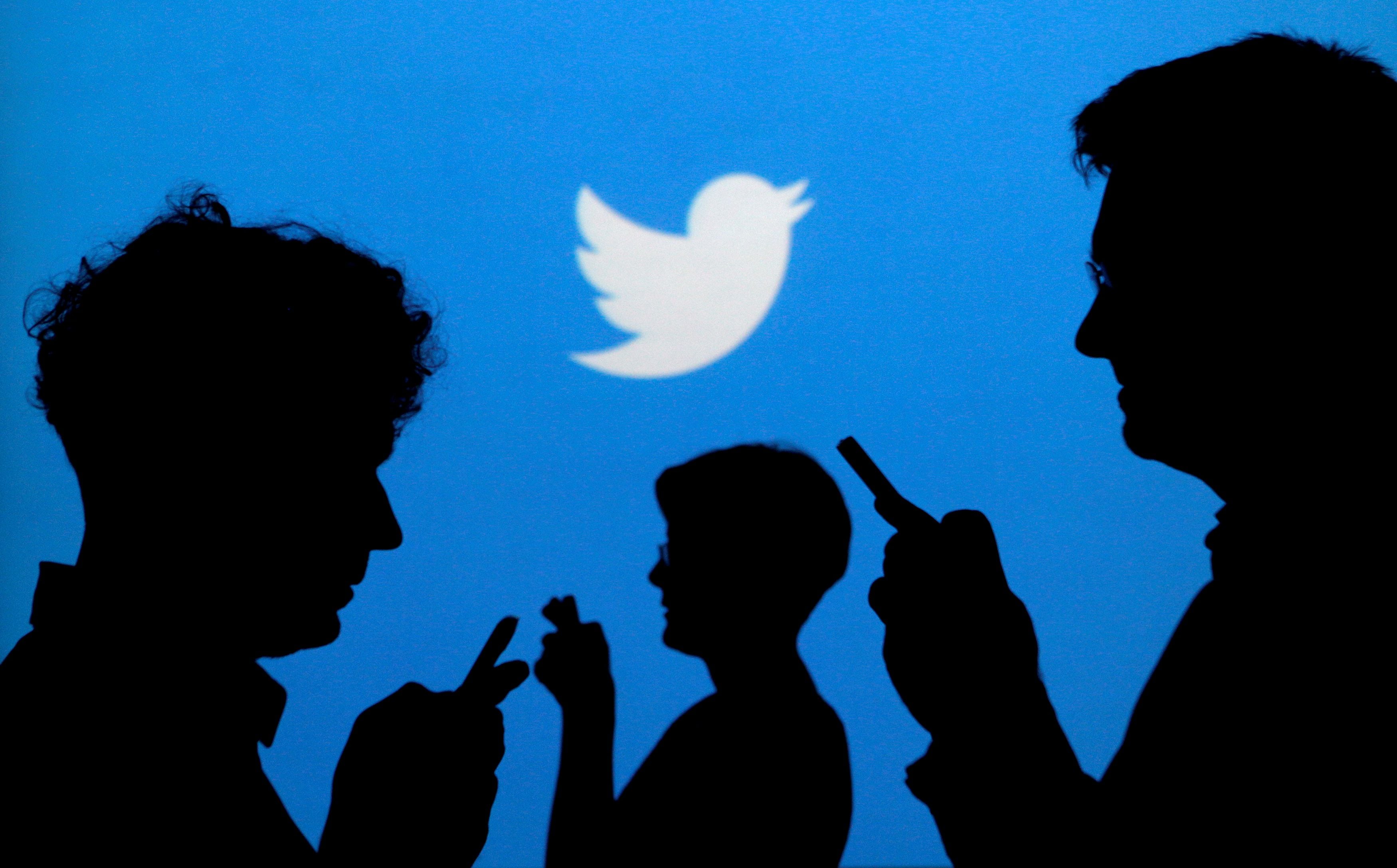 FILE PHOTO: Smartphone users are silhouetted against a backdrop projected with the Twitter logo