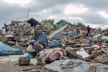 A tsunami survivor sits on a pice of debris as she salvages items fro