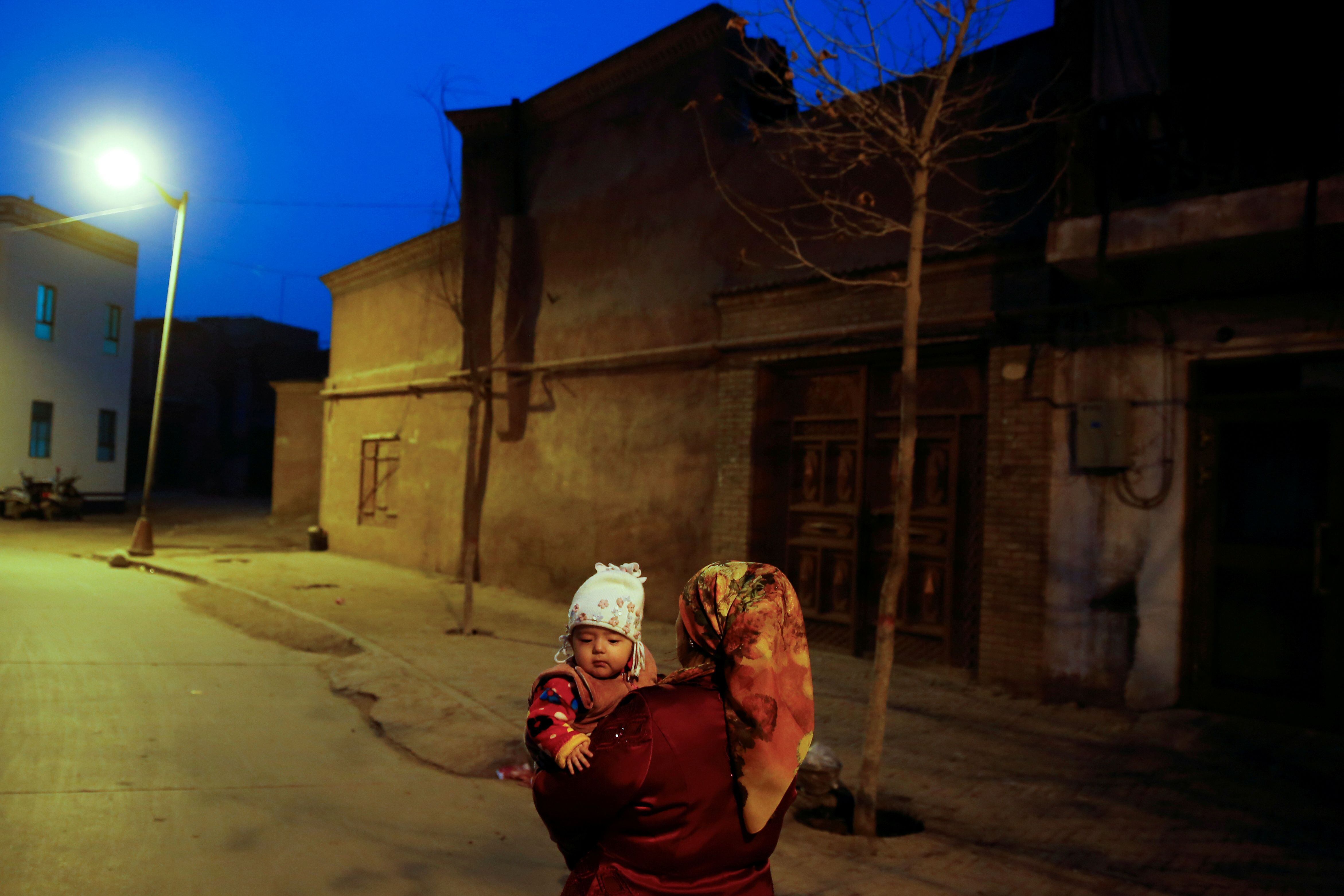 FILE PHOTO: A woman carries a child at night in the old town of Kashgar