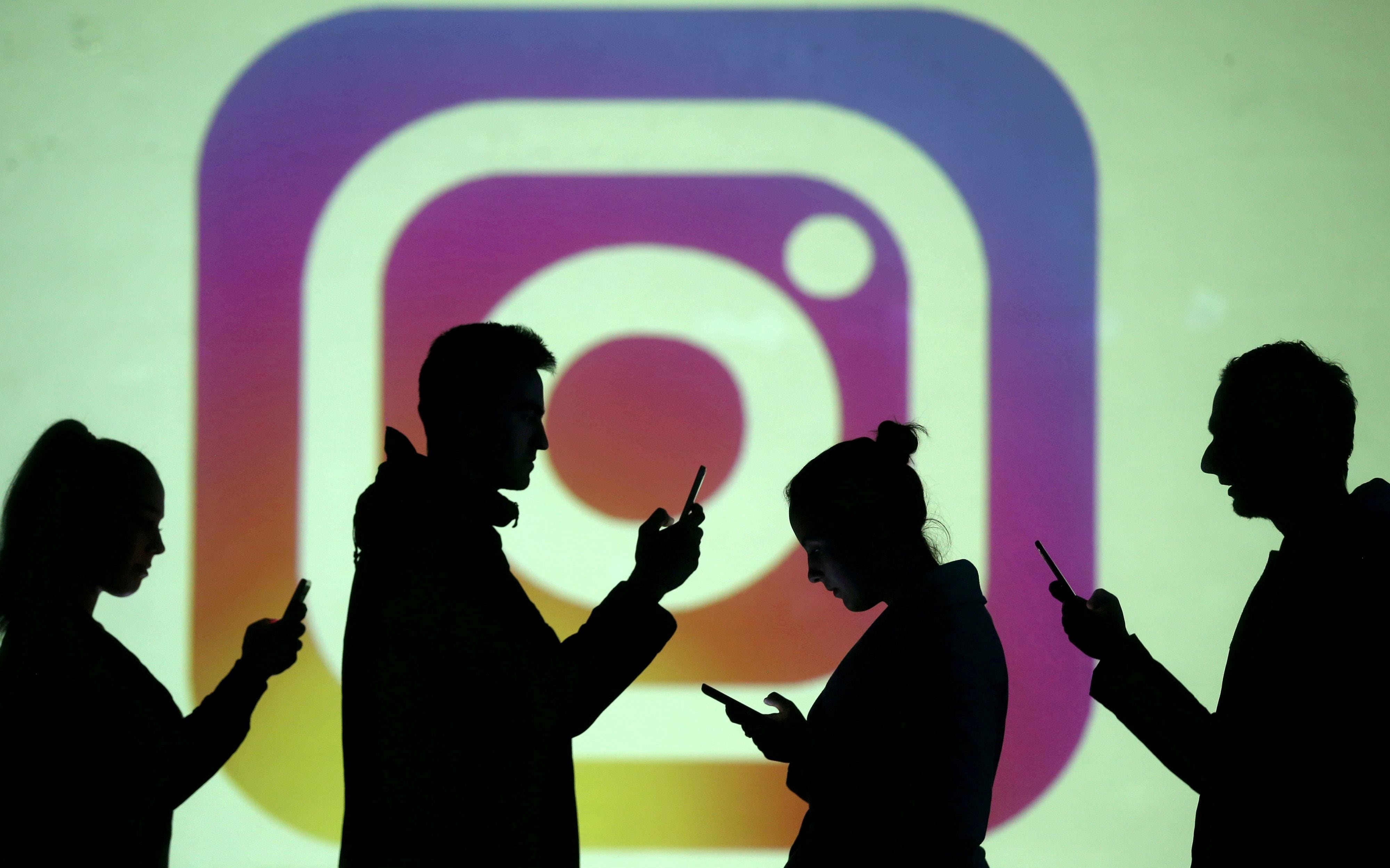 FILE PHOTO: Silhouettes of mobile users are seen next to a screen projection of Instagram logo in this picture illustration