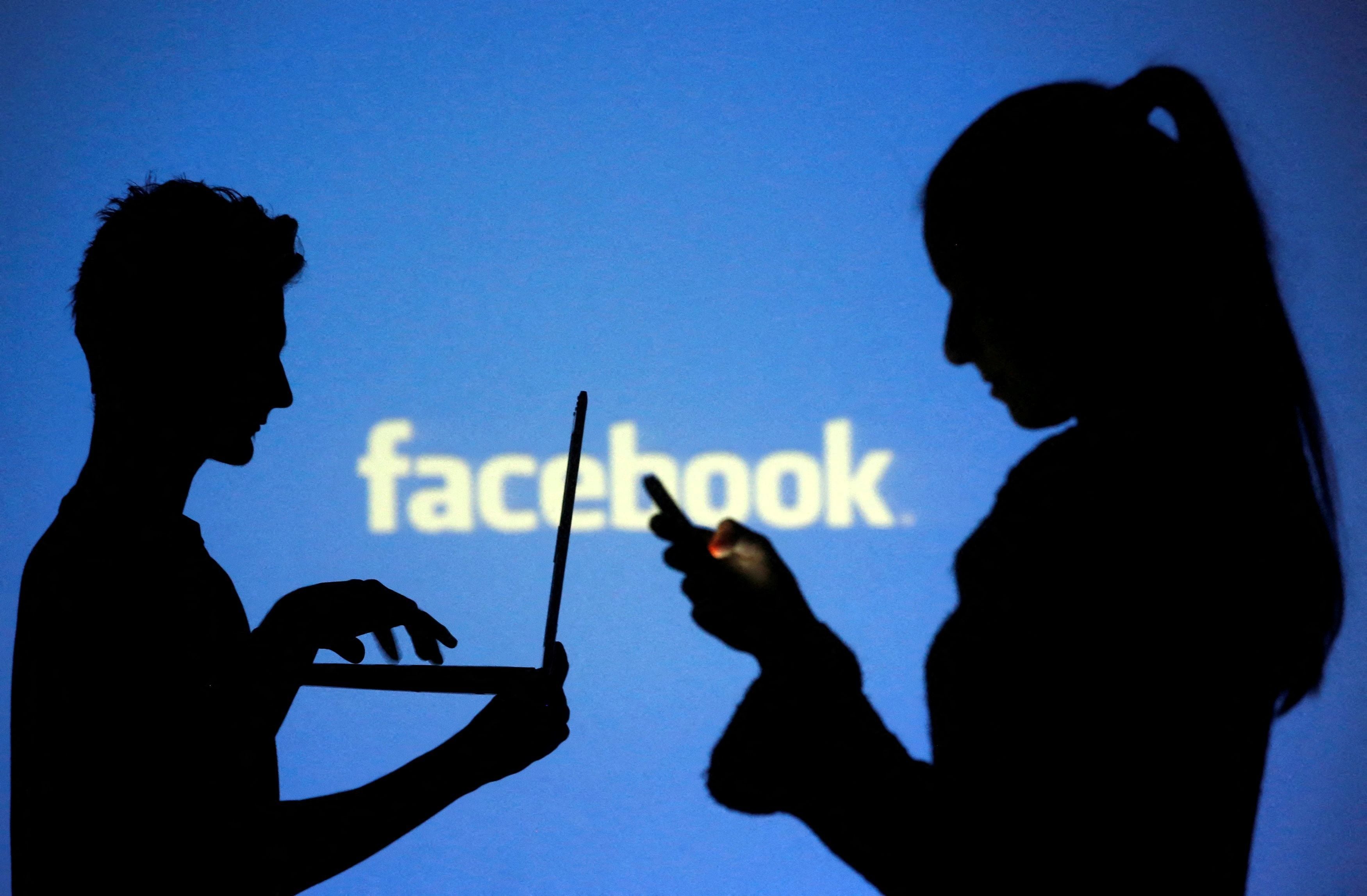 FILE PHOTO: People pose with laptops in front of projection of Facebook logo in this picture illustration taken in Zenica