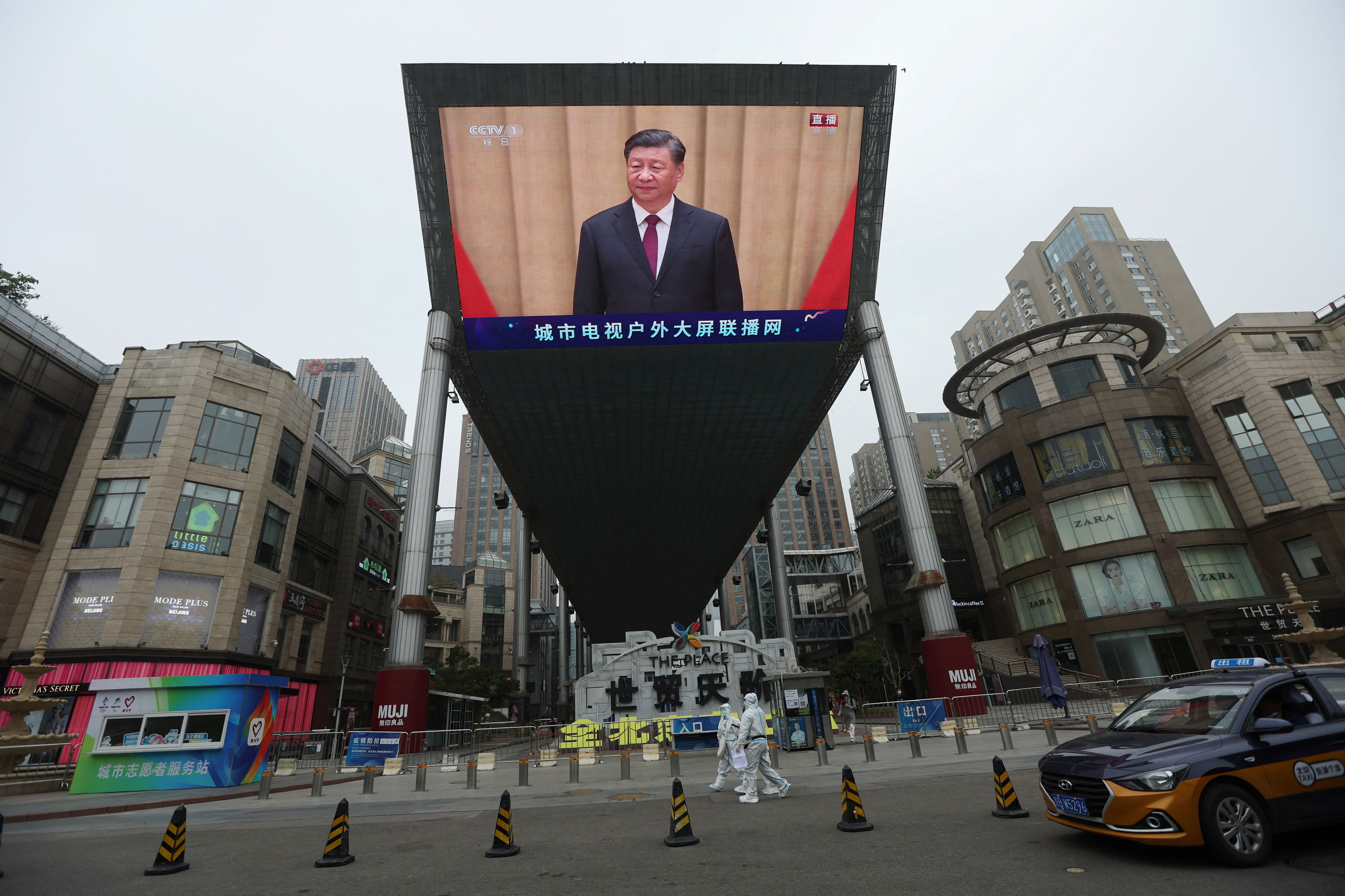 Medical workers in protective suits walks past a giant screen showing Chinese President Xi Jinping in Beijing