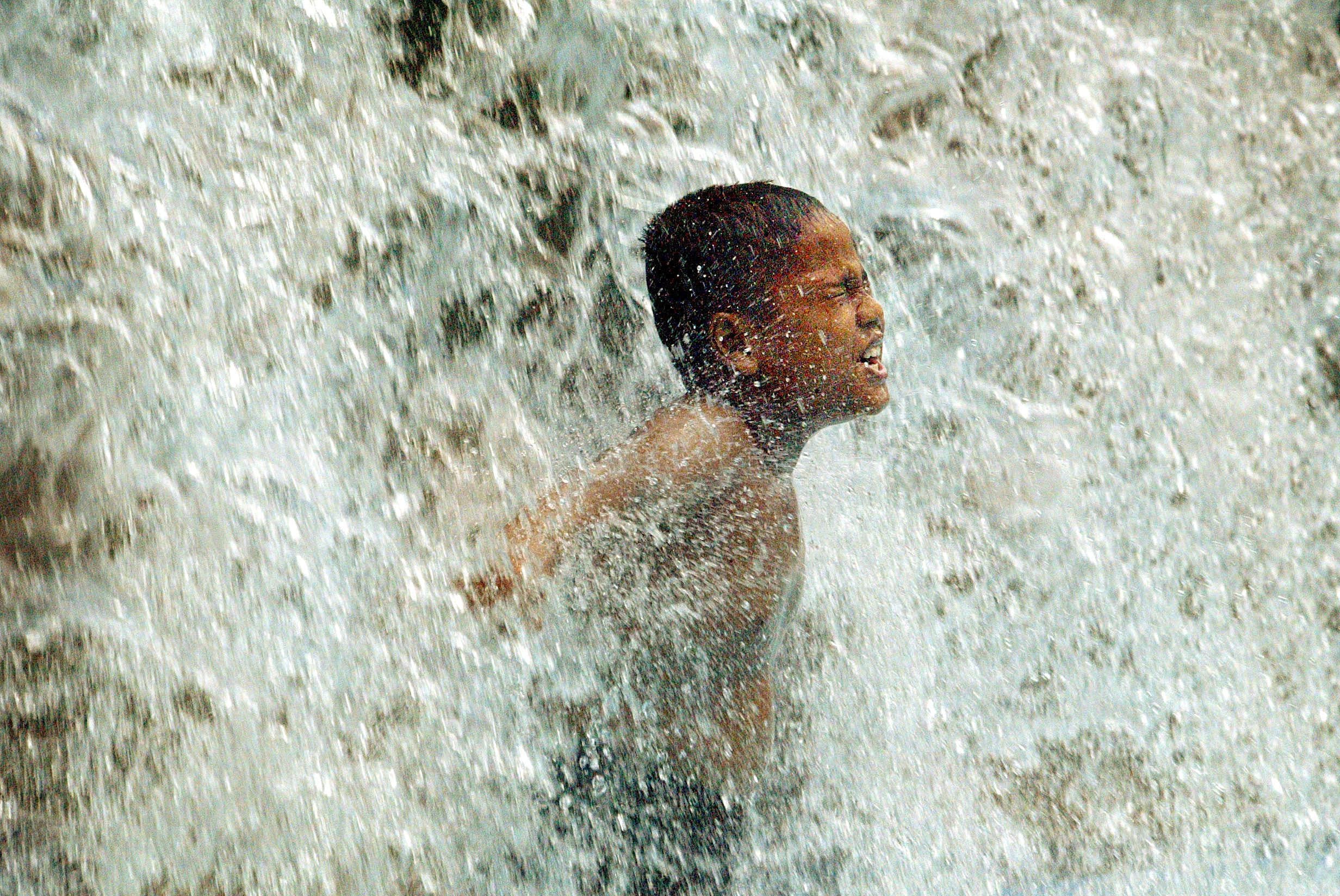 A MALAYSIAN BOY PLAYS IN A WATERFALL IN KUALA LUMPUR.