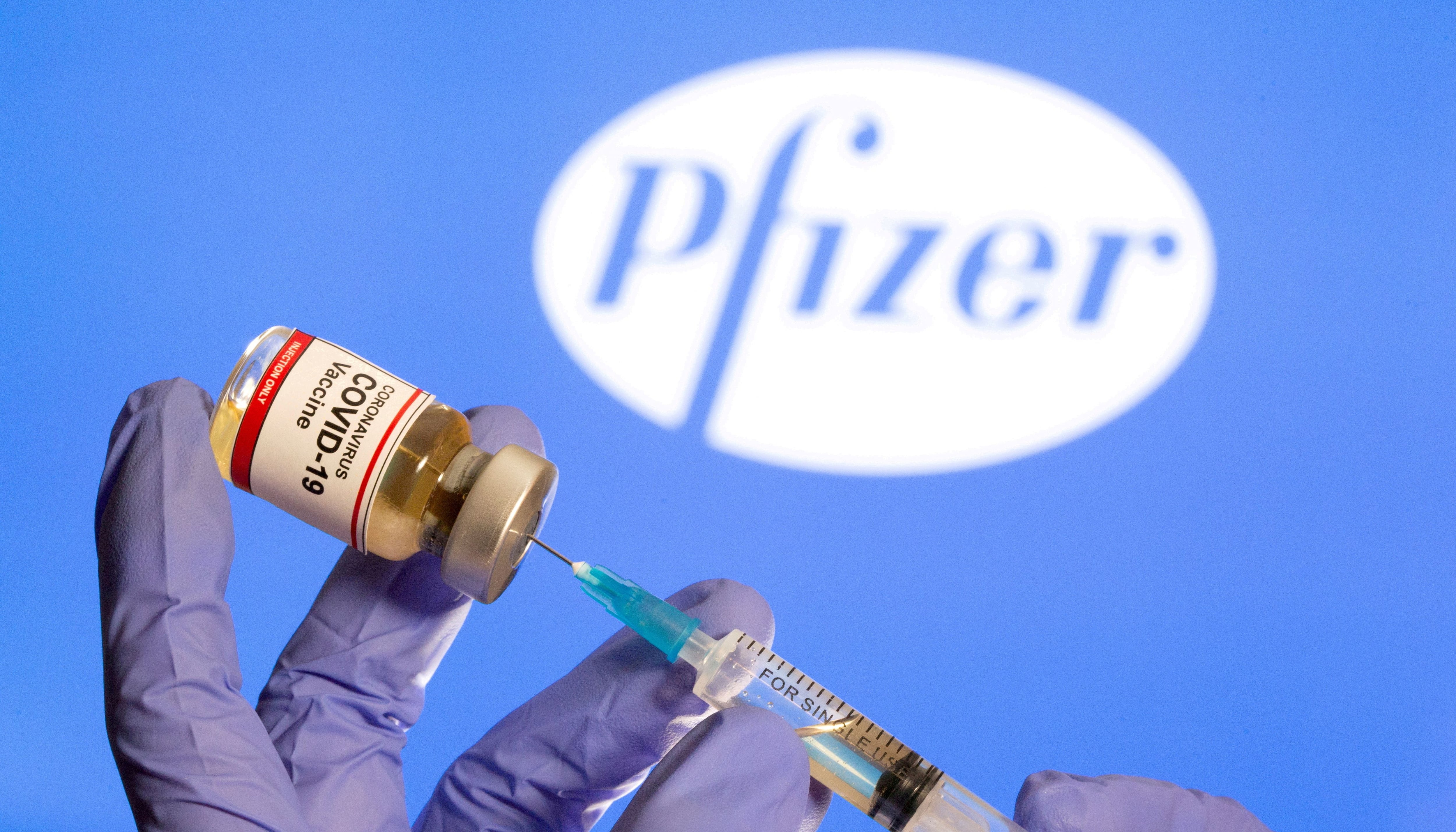 FILE PHOTO: A woman holds a small bottle labeled with a 'Coronavirus COVID-19 Vaccine' sticker and a medical syringe in front of displayed Pfizer logo in this illustration